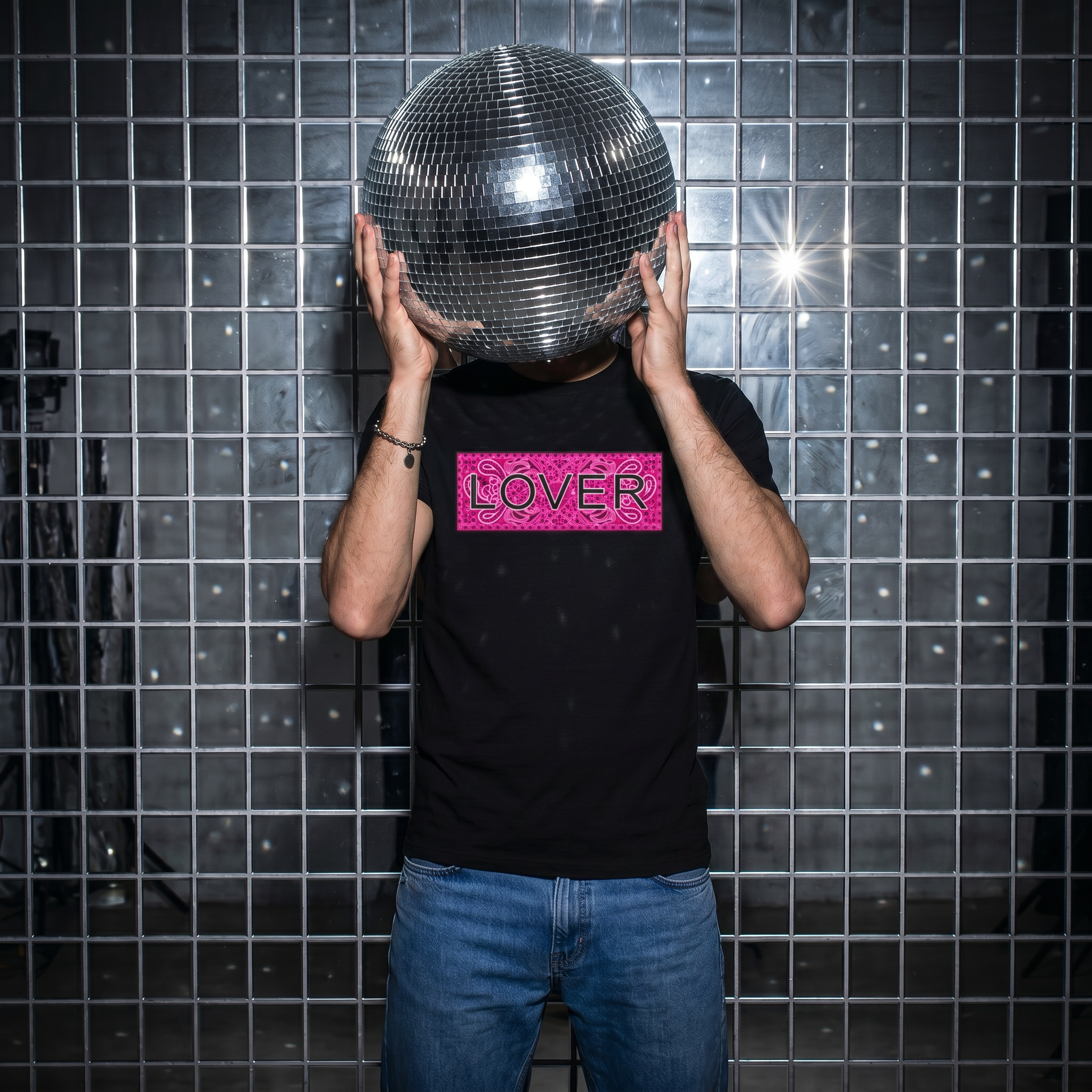 Person holding a disco ball in front of their head against a tiled wall with 'LOVER' shirt.